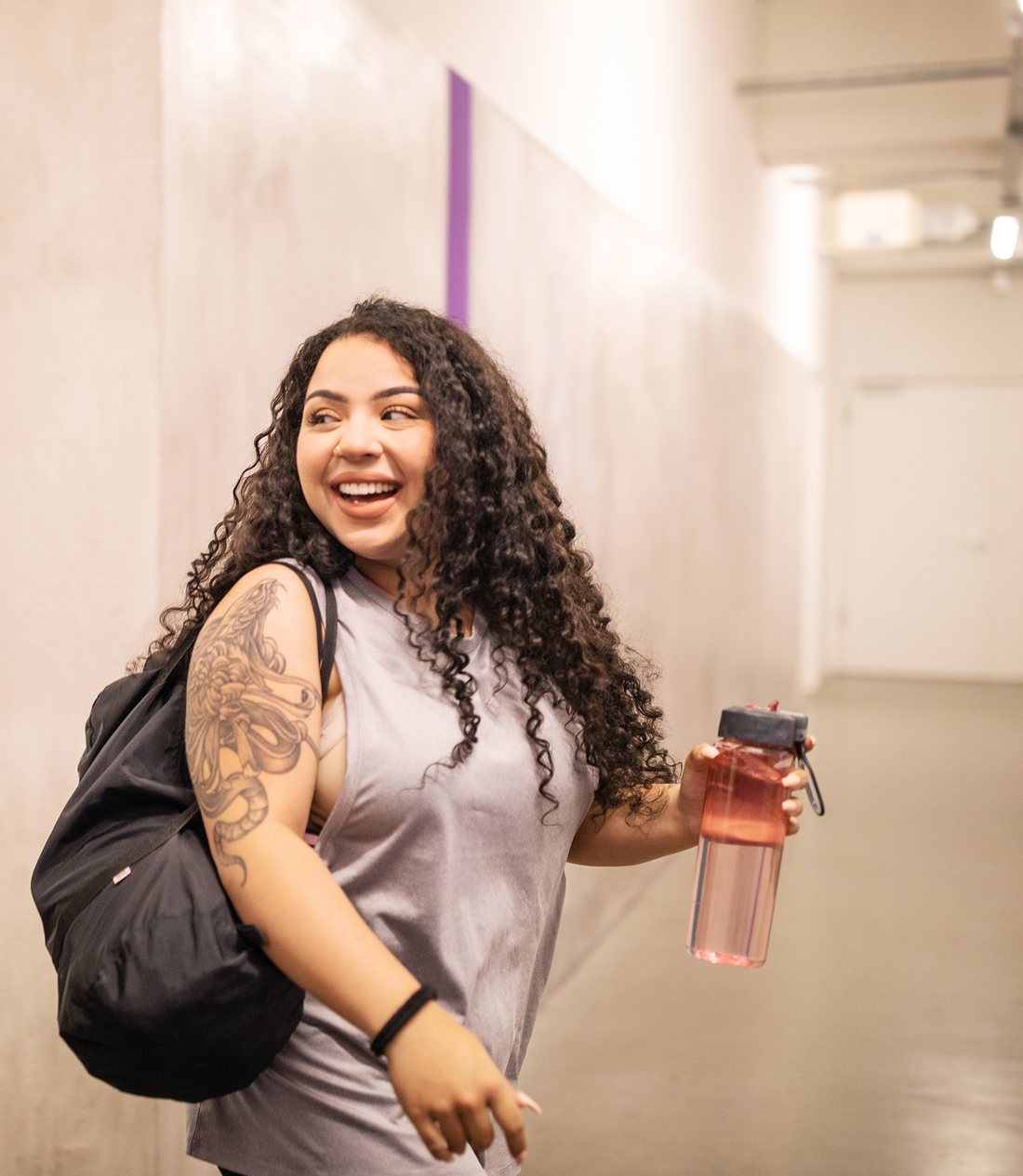 Étudiante souriante remplissant sa gourde réutilisable dans un corridor