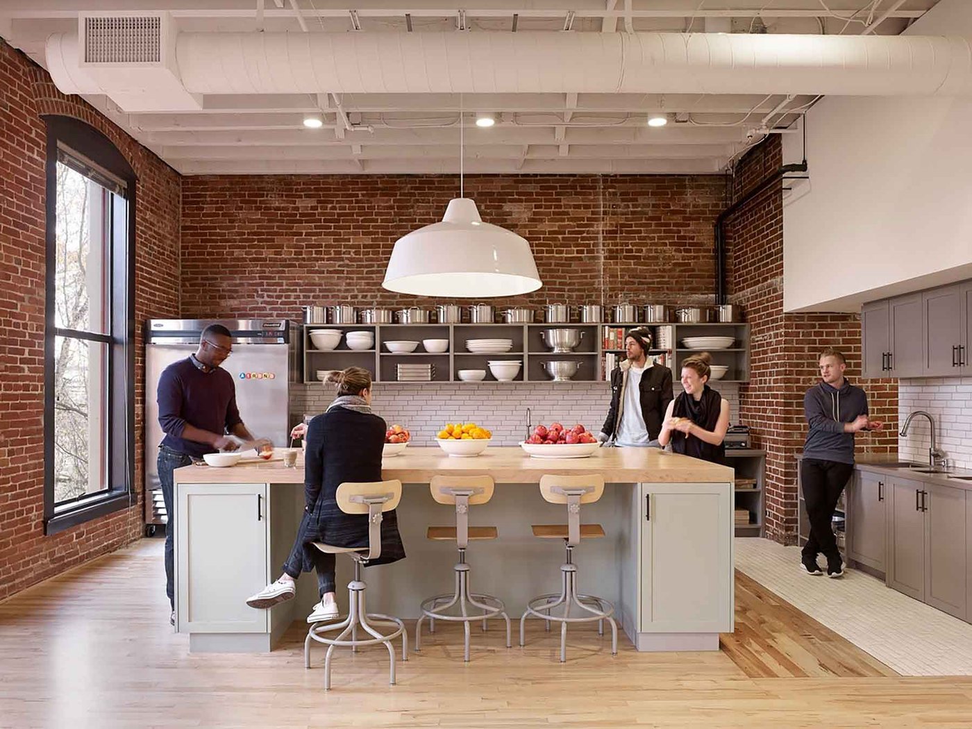 Employés réunis autour de l'îlot de la cuisinette d'un bureau moderne au mur de briques